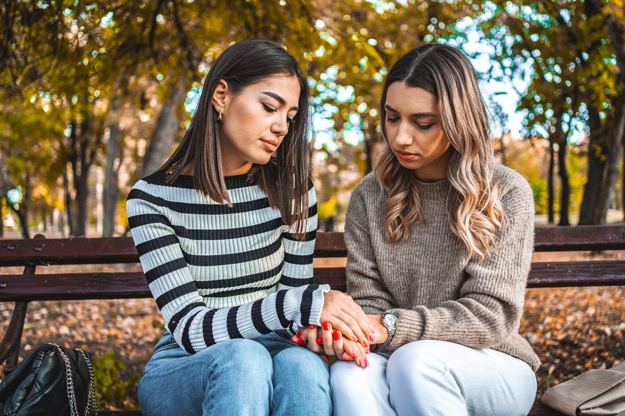 Young woman comforting her sad friend in the park during autumn