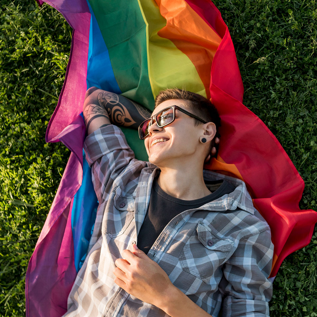 cheerful young person lying on a lgbt flag on the grass