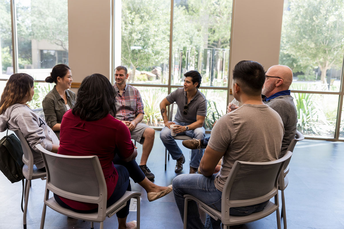 Diverse group of adults sitting in a circle, engaging in supportive conversation indoors